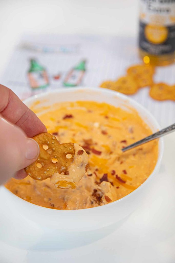 Dipping into Microwave Beer Cheese Dip with a pretzel thin in a cereal bowl